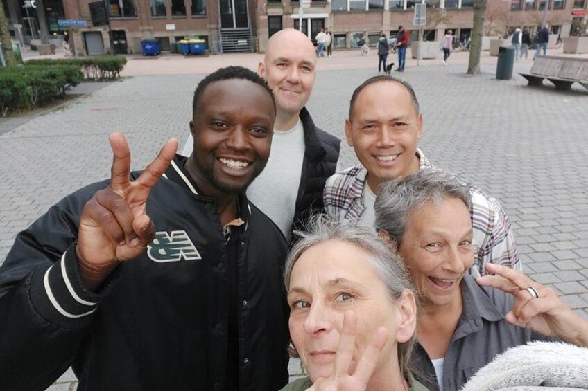 A group of people posing for a photo in an urban setting with buildings and a paved area in the background. 3