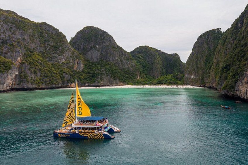 A boat with a yellow sail on turquoise water surrounded by green cliffs. 1