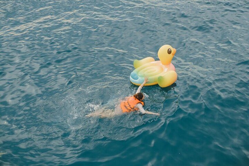 A person swimming in water with a yellow duck float. 4