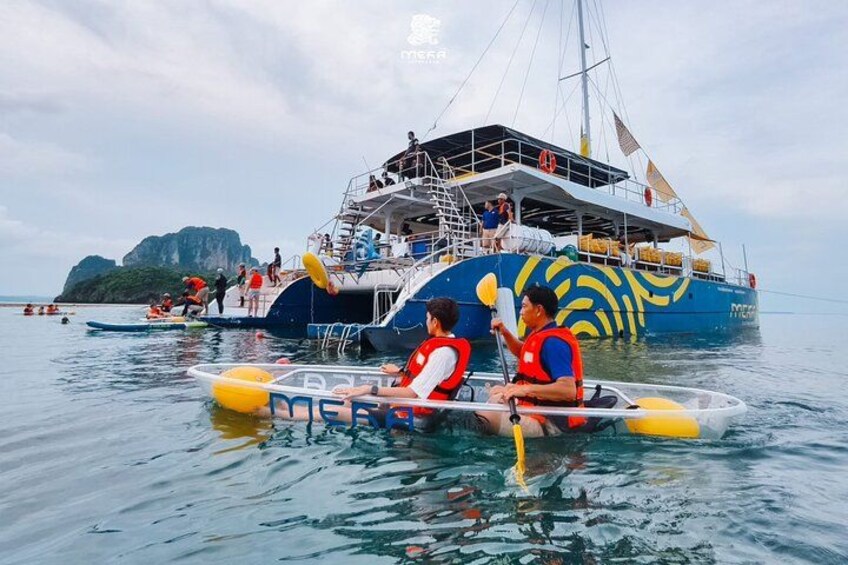 A boat with people paddling in the water, a large ship in the background, and a rocky island. 3