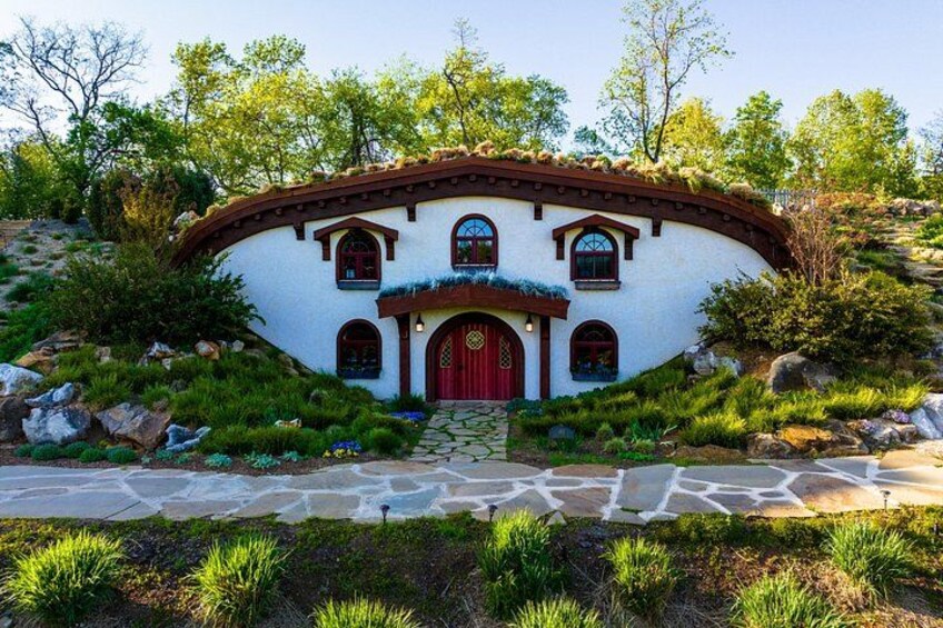 A white house with a red door, surrounded by greenery and rocks. 3
