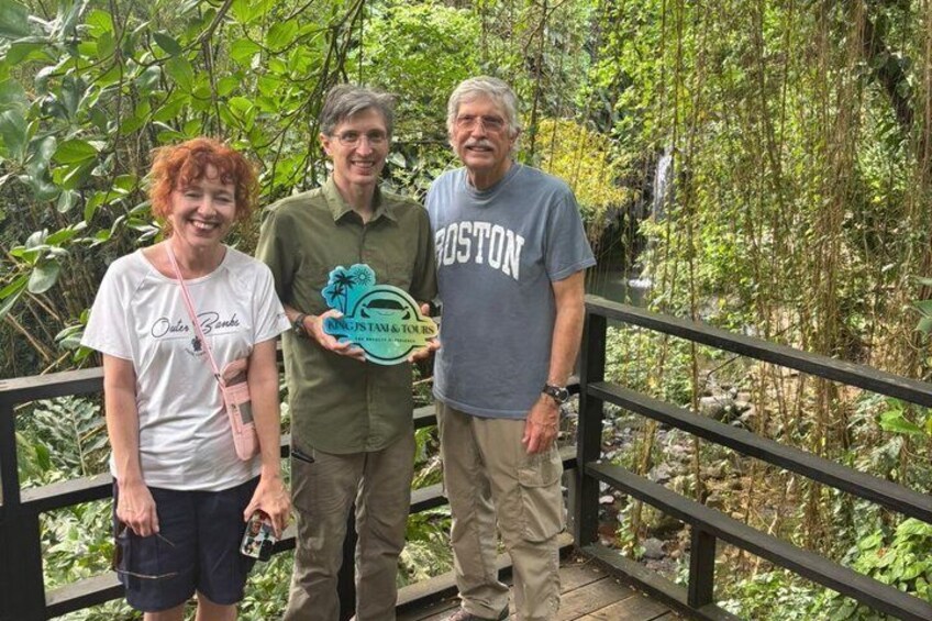 Tres personas caminando sobre un puente de madera, con follaje verde al fondo. 2