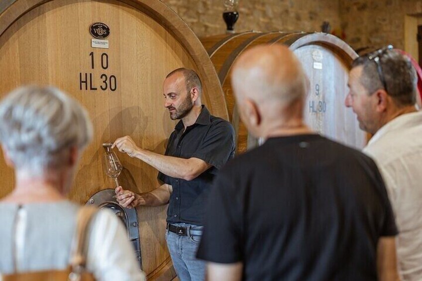 Un hombre sostiene una copa de vino en una bodega con barriles de madera etiquetados con números. 1