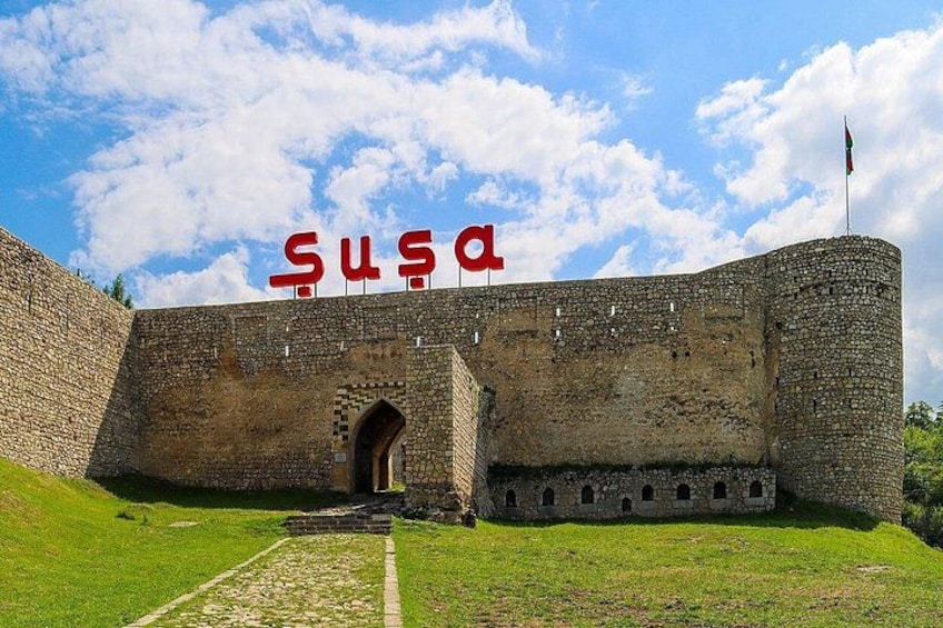Una fortaleza de piedra histórica con un amplio arco de entrada, una bandera en la cima y un primer plano cubierto de césped. 1