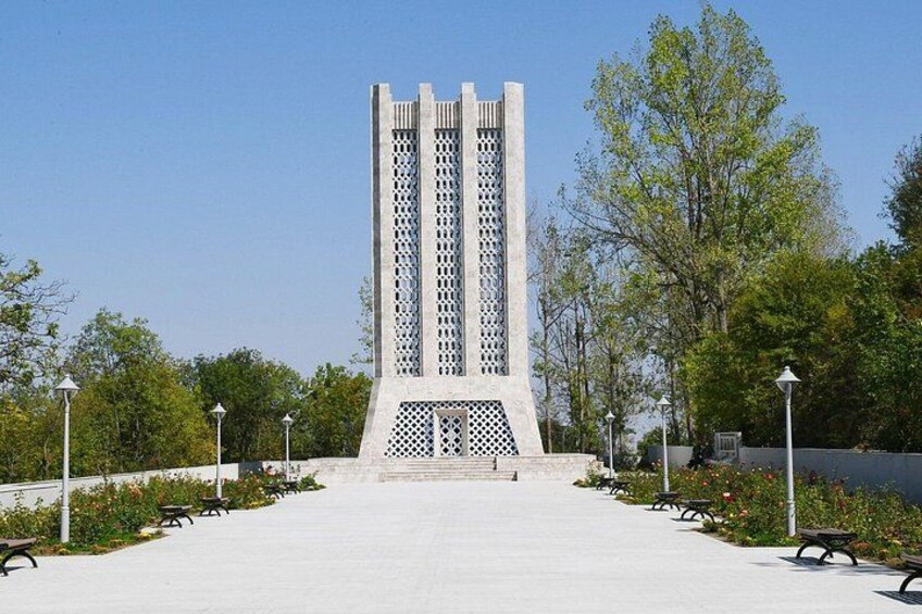 Una torre alta de estilo modernista con diseño de celosía, rodeada por un paseo empedrado con bancos y farolas. 3
