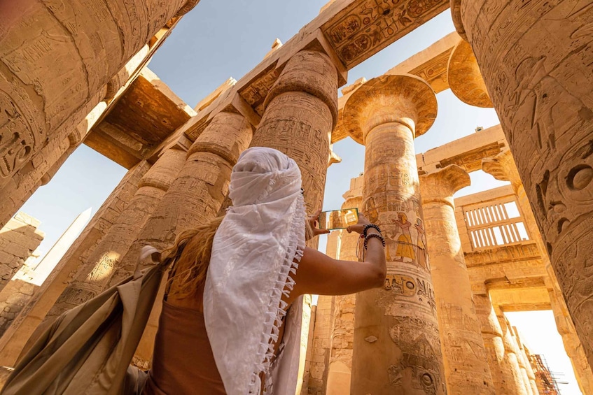 A person taking a photo inside an ancient Egyptian temple with large columns and hieroglyphs. 1