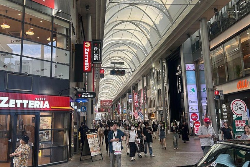 A busy indoor shopping mall with a glass ceiling, various stores, and people walking. 3