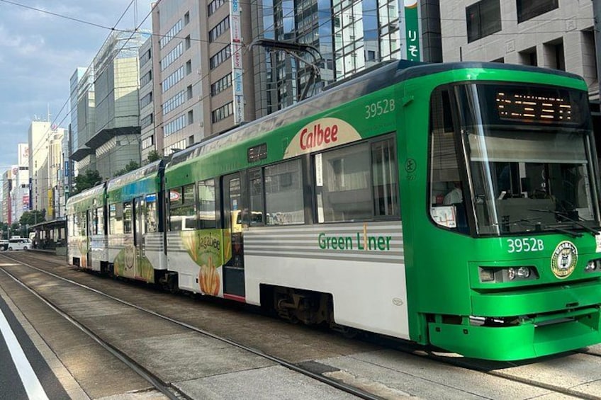 A green and white tram with advertisements on its side, traveling on a track in an urban setting. 2
