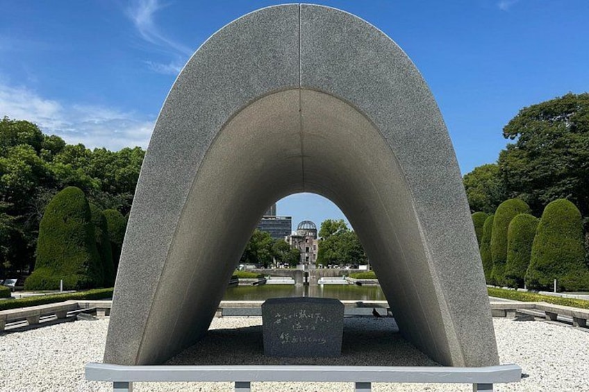 A large concrete arch monument with a plaque in the center, surrounded by a park with trimmed trees and a distant building. 5