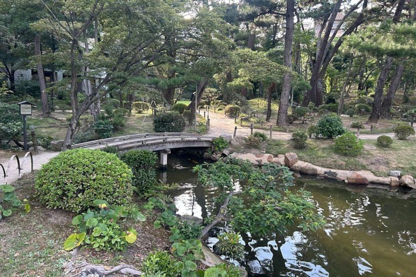 A traditional Japanese garden with a stone bridge, water features, and lush greenery. 1
