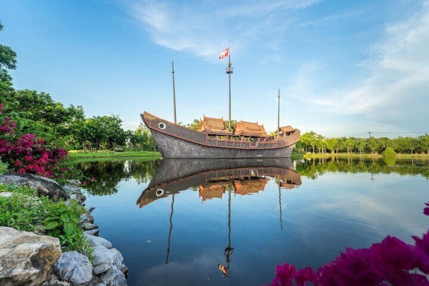 A traditional wooden boat with a flag, docked in a calm lake surrounded by greenery. 2