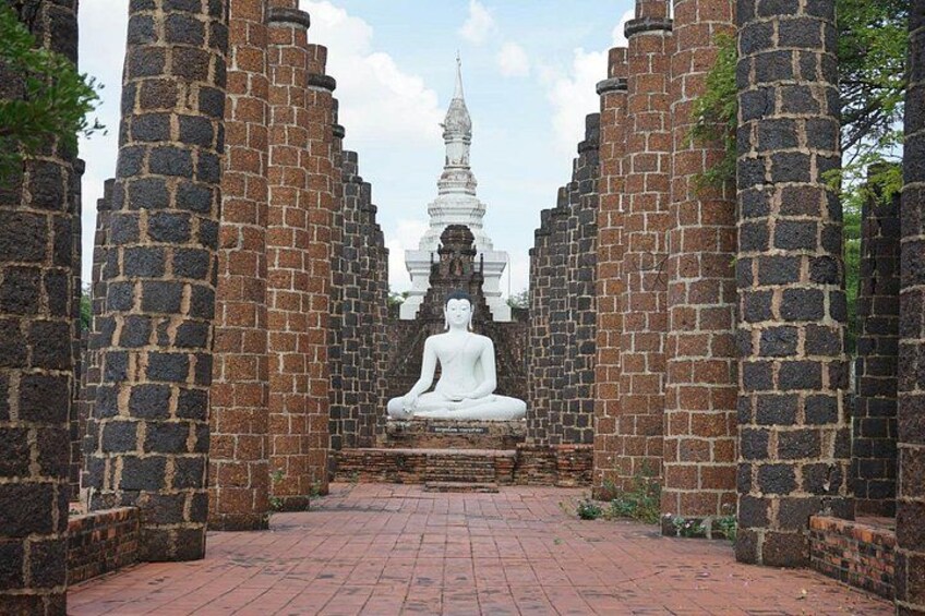En hvid statue af en siddende figur i en templegang med murstensvægge og en murstenssti. 3