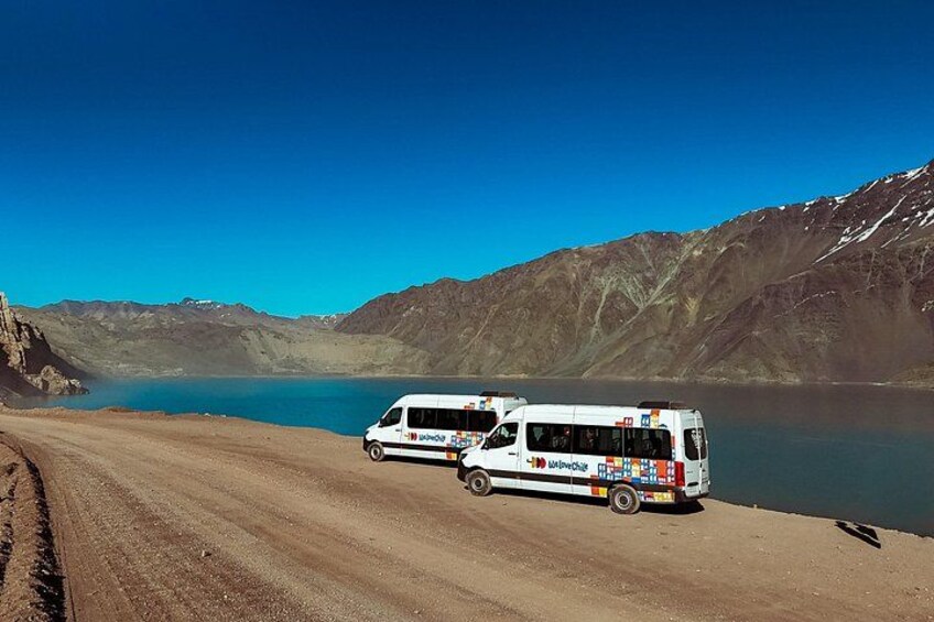 Una camioneta blanca estacionada junto a un lago con montañas al fondo. 2