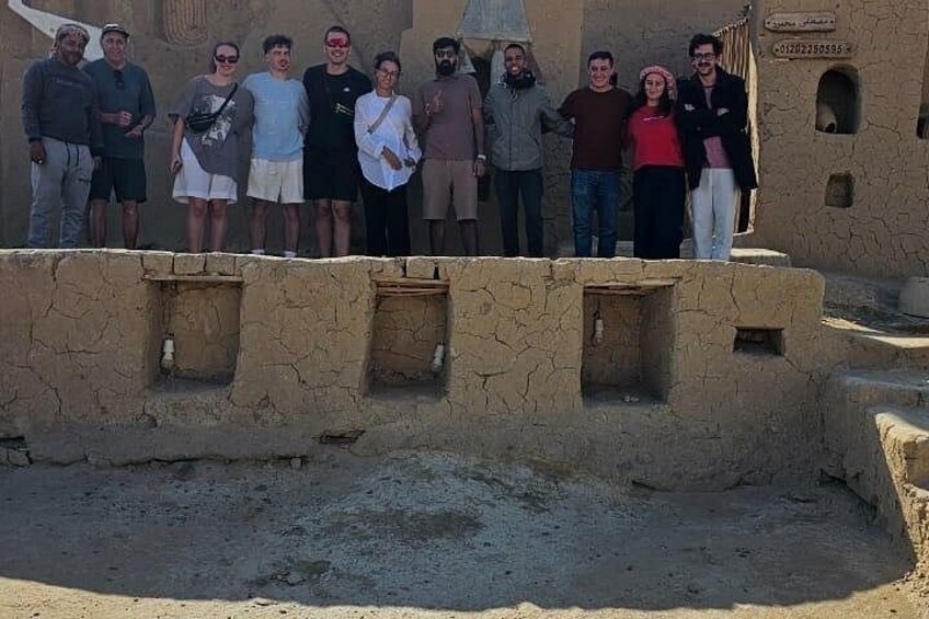 Un groupe de personnes se tient devant une structure ancienne, dotée d’un toit plat et de petites ouvertures. 5