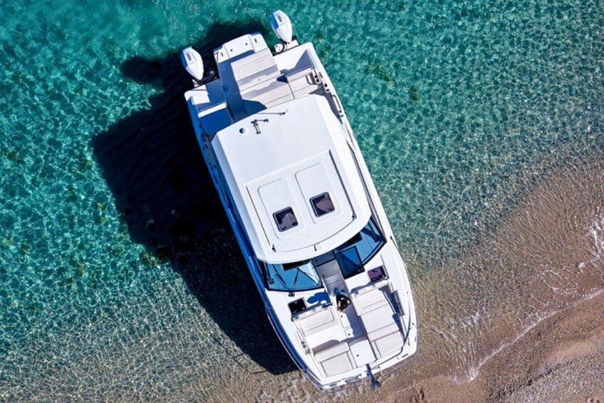 An aerial view of a white boat with blue accents docked on a beach with clear turquoise water. 2