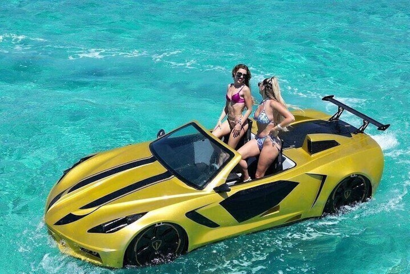 Une voiture de sport jaune, avec deux personnes en maillot de bain sur le toit, flottant sur une eau turquoise. 1