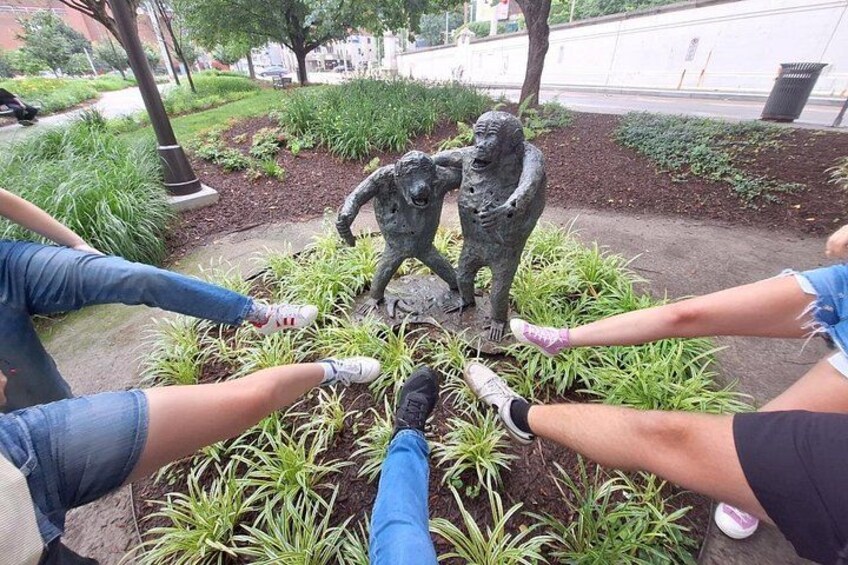 People sitting on a bench with a statue of two figures in the center. 4