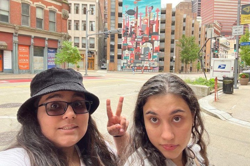 Two people taking a selfie with a city street and buildings in the background. 2