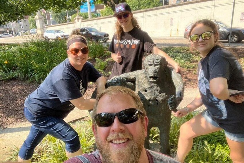 A group of people posing with a stone statue in a park. 1