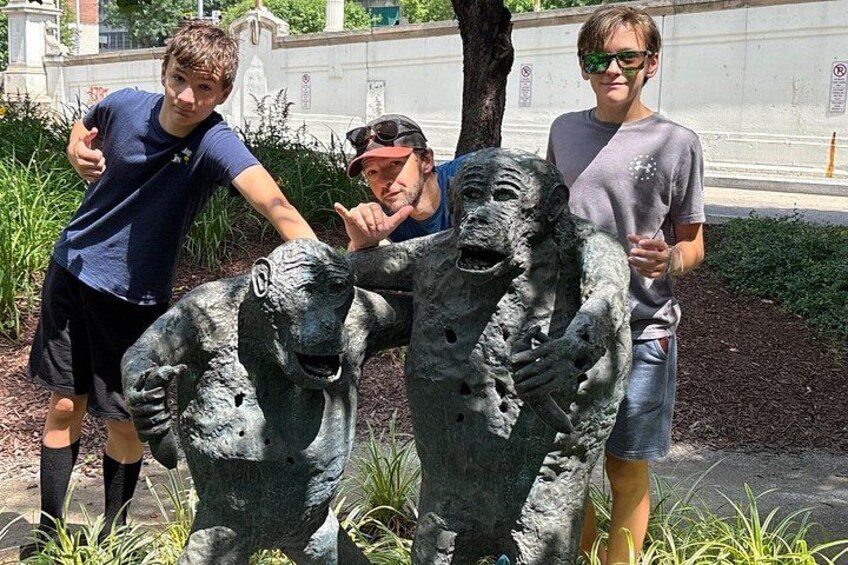 A group of people posing with a sculpture of gorillas in a park. 5