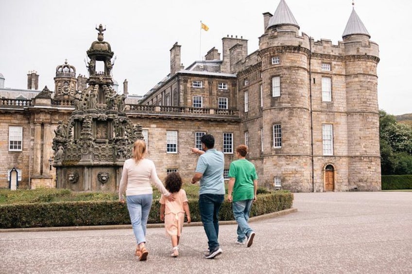 A family walking in front of a historic castle with intricate architecture and a large fountain. 1