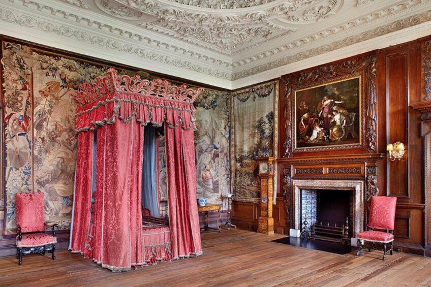 A grand room with a four-poster bed, ornate wall paintings, and a fireplace. 3