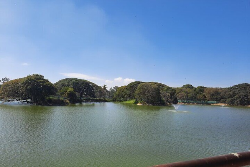 Un lago tranquilo con una fuente, rodeado de árboles frondosos y un cielo azul despejado. 1