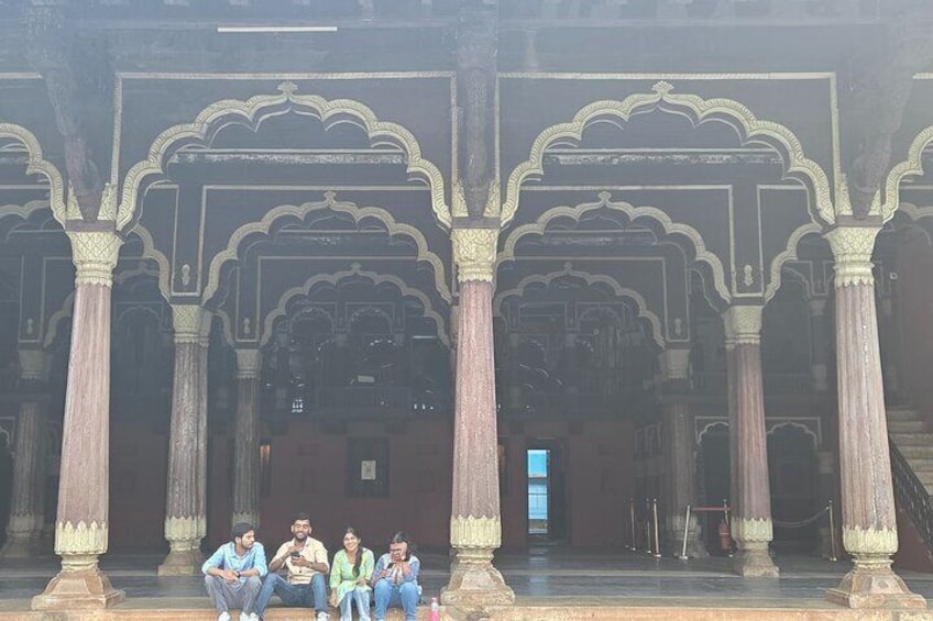 Un grupo de personas sentadas en un banco en un patio con arcos y columnas decorativas. 3