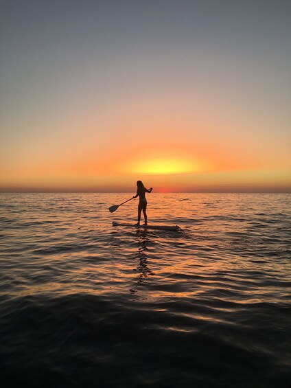 A person paddleboarding on calm water during sunset. 5