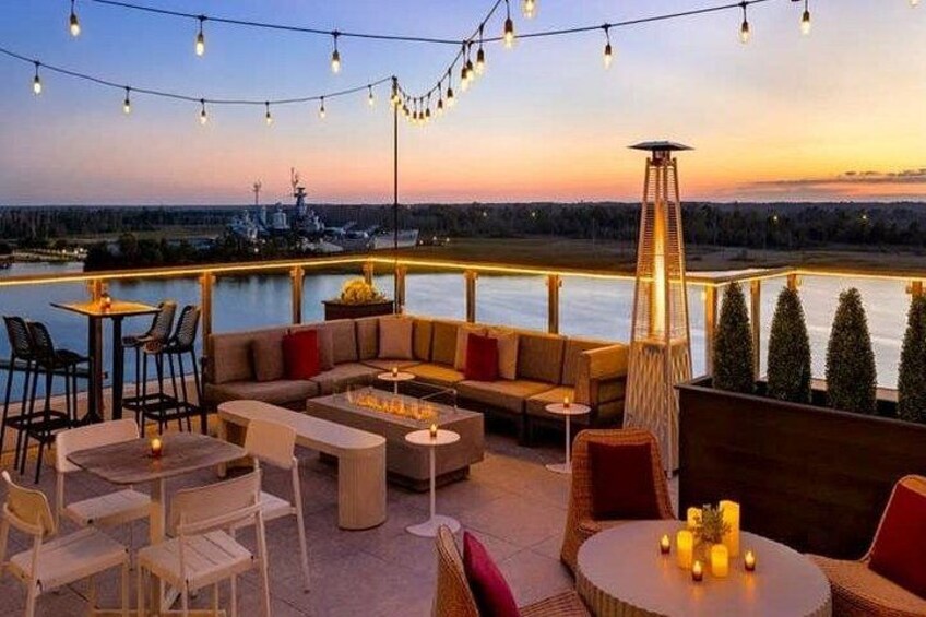 An outdoor seating area with tables, chairs, and a sofa, overlooking a body of water. 2