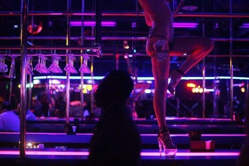A person performing an acrobatic act in a dimly lit venue with a bar and audience in the background. 3