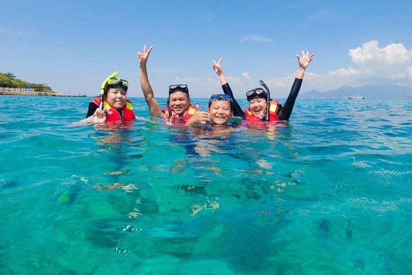 Four people snorkeling in clear blue water with a boat in the distance. 4