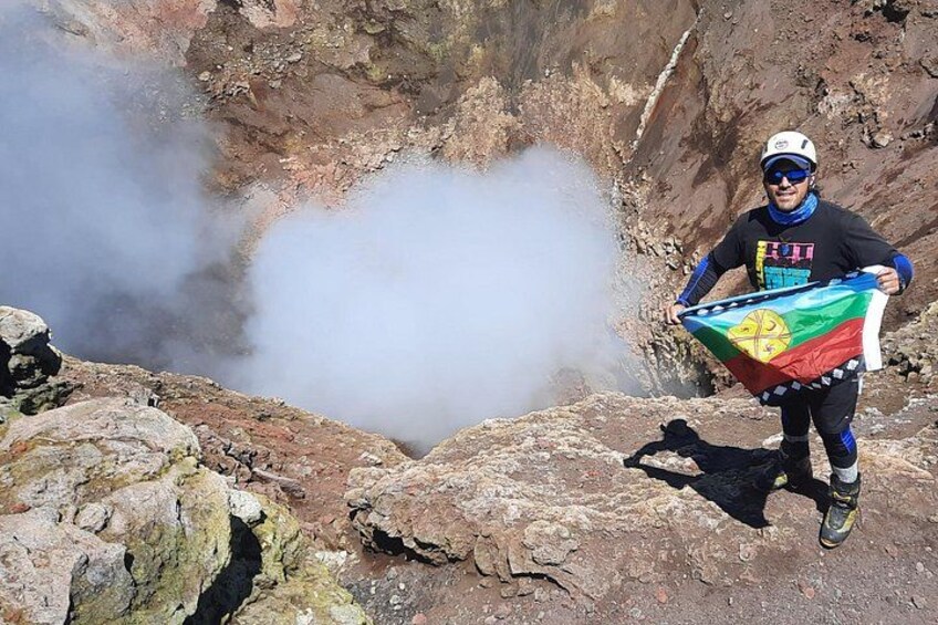 A person standing on rocky terrain with a flag, surrounded by a steep cliff and steam rising from a crevice. 3
