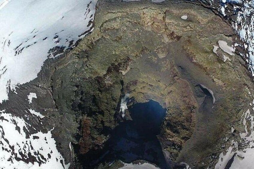 A large glacier with a deep blue center, surrounded by snow-covered terrain and patches of vegetation. 2