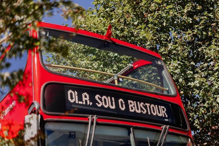 A red bus with a sign that reads 'OLA, SOU O BUSTOUR' on the front. 2