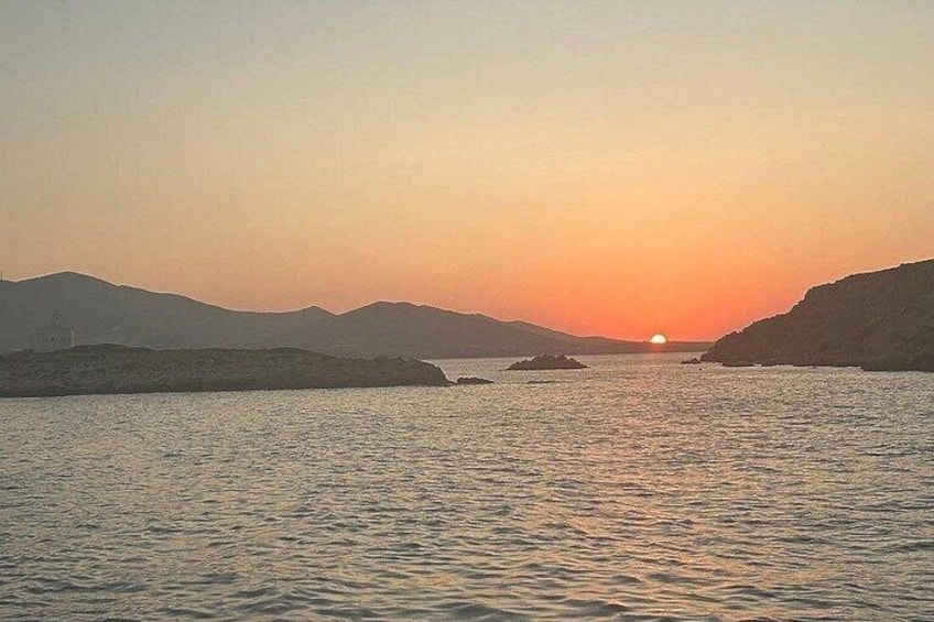 A sunset over a calm sea with distant hills and a lighthouse. 5