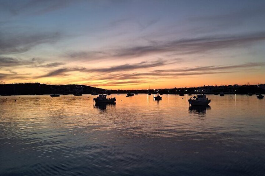 A calm harbor at sunset with boats anchored in the water. 2