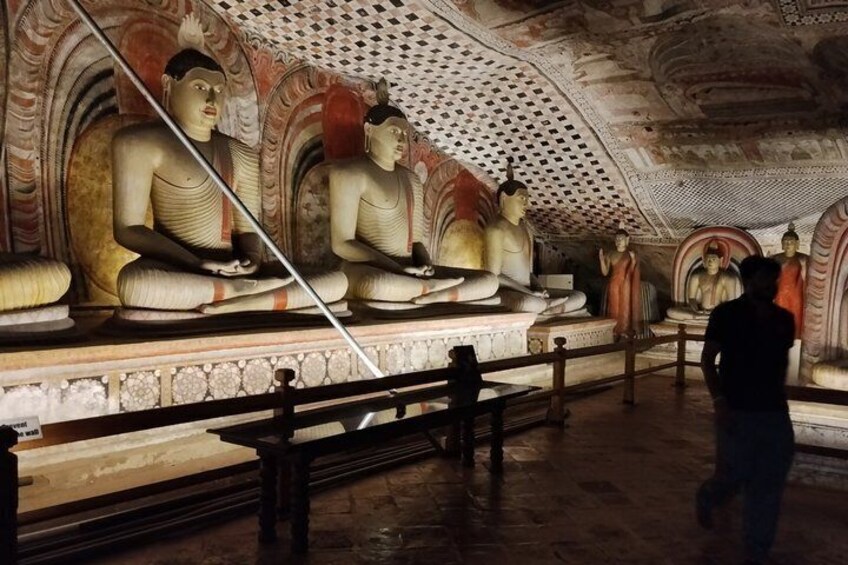 A temple interior with large seated Buddha statues and intricate ceiling artwork. 2