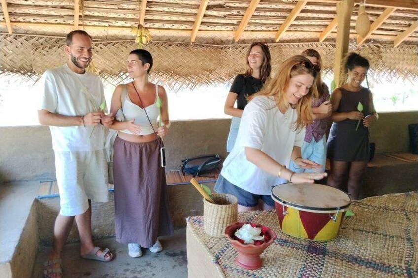 A group of people playing drums in a rustic outdoor setting with a thatched roof. 5