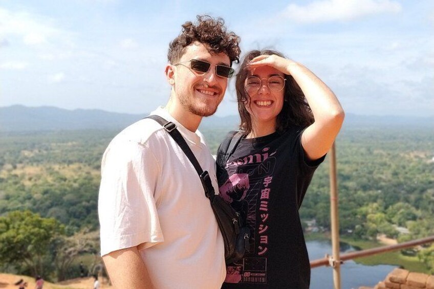Two people standing on a high vantage point overlooking a landscape with trees and a body of water. 3