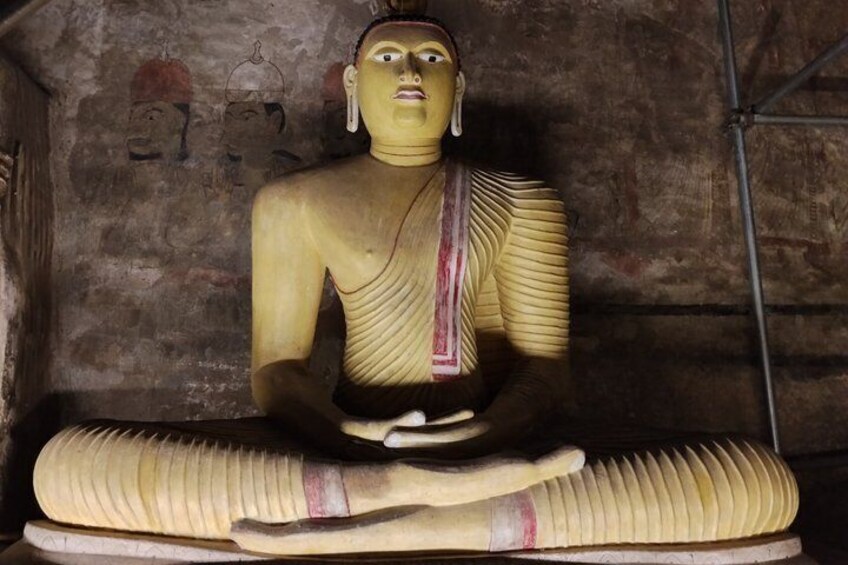A seated statue with a striped garment, set against a textured wall with faint drawings. 4