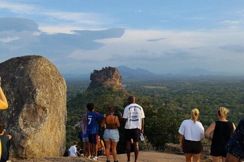 A group of people standing on a viewing platform overlooking a mountainous landscape with a prominent rock formation. 2