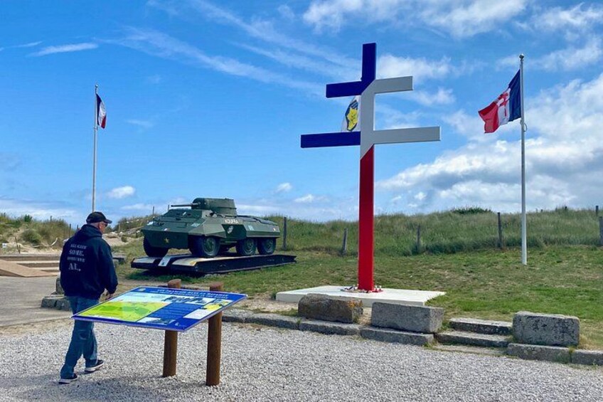 A cross-shaped monument, a military tank, and a map stand with a person standing nearby. 2