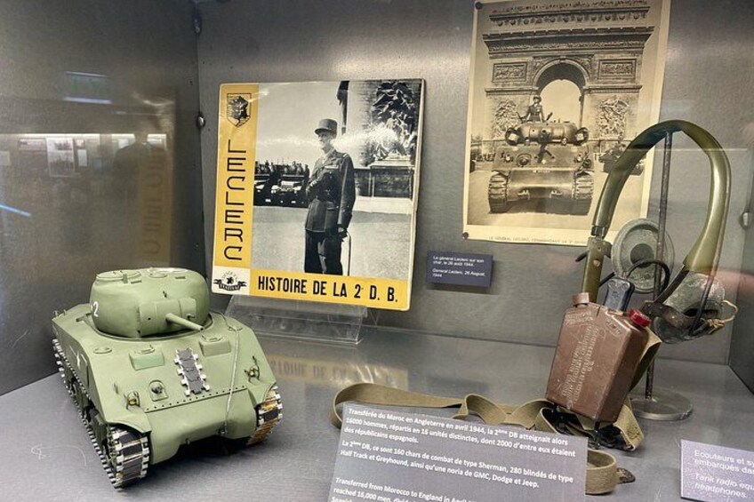 A military display with a green tank, a historical poster, and a French monument. 3
