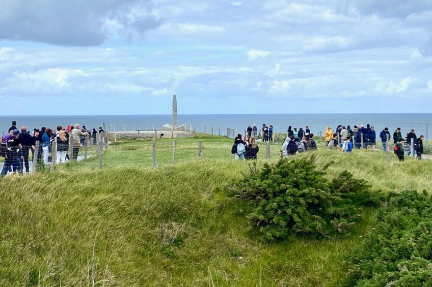 A coastal landscape with a grassy area, a fence, and a distant monument. 1