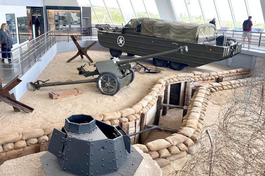 A military exhibit with a tank, sandbags, and a bunker-like structure. 5
