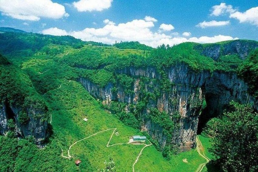 A lush green valley with a prominent rock formation and a small building. 2