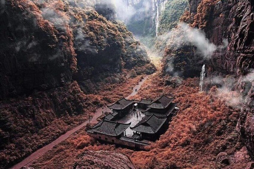 A traditional building with a tiled roof surrounded by red foliage and rocky cliffs. 3