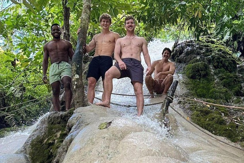 Cuatro personas sobre una formación rocosa con una cascada en un área boscosa. 3