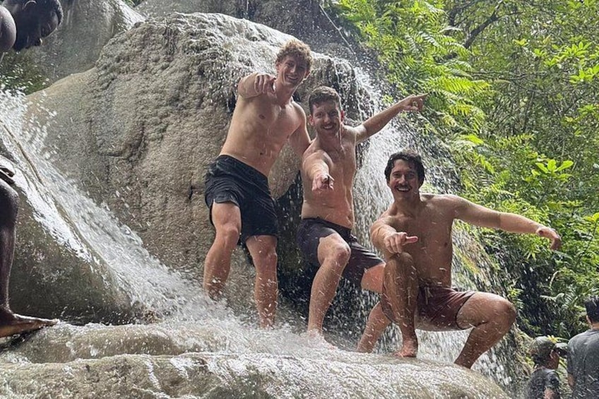Tres personas saltando a una cascada rodeada de rocas y vegetación. 4